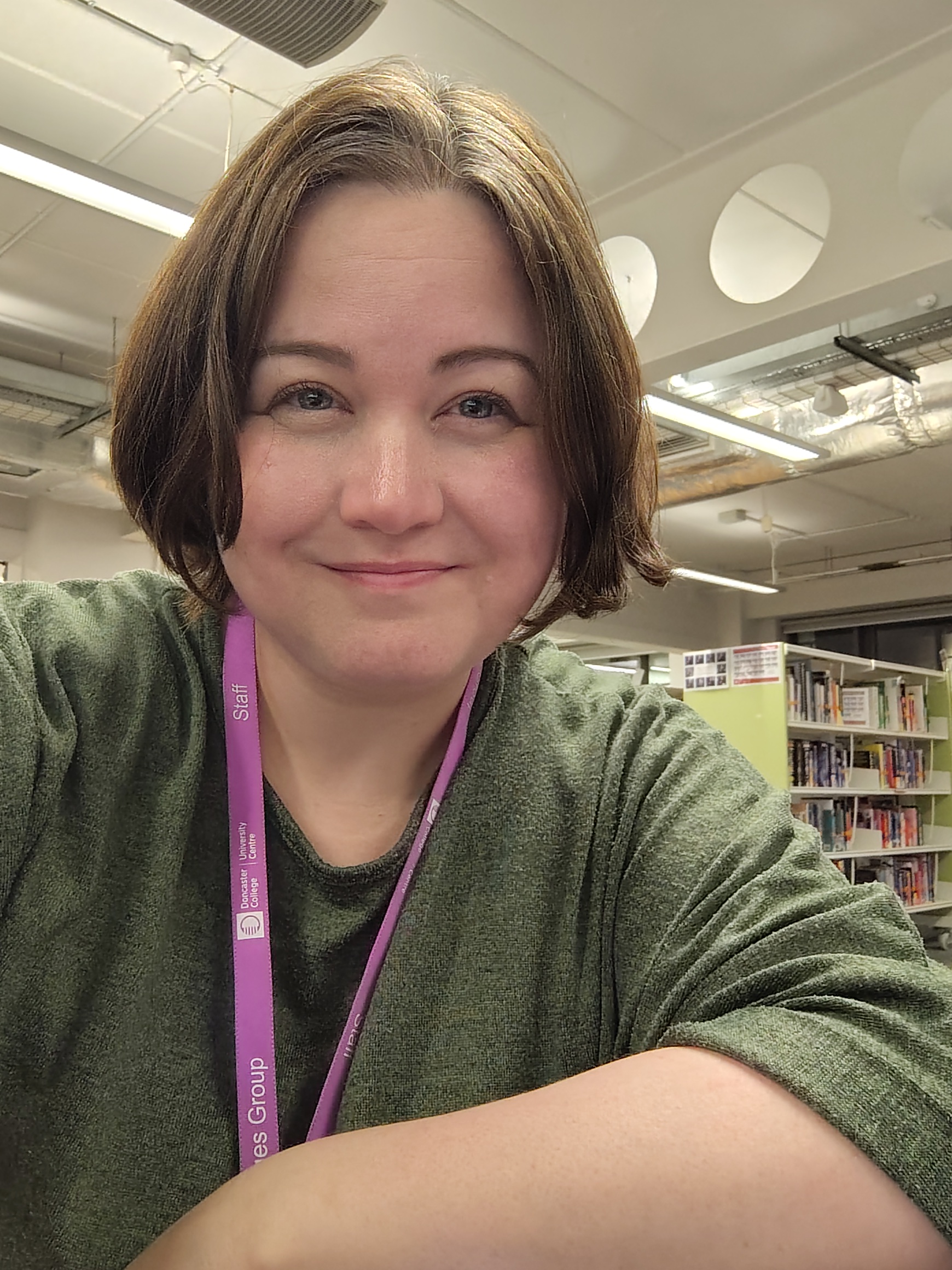 A smiling person in a library wearing a lanyard